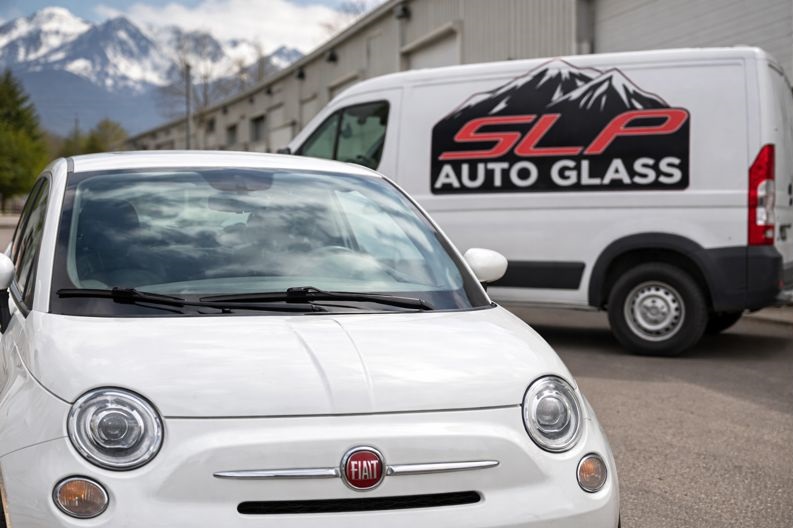 White Fiat 500 with visible Fiat emblem parked in front of an SLP Auto Glass service van.