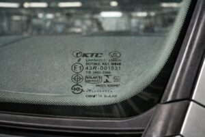Auto glass certification mark etched at the bottom center of a vehicle windshield showing DOT, AS1, E1, and laminated safety glass markings.