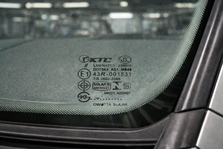 Auto glass certification mark etched at the bottom center of a vehicle windshield showing DOT, AS1, E1, and laminated safety glass markings.