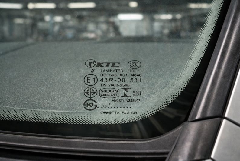 Auto glass certification mark etched at the bottom center of a vehicle windshield showing DOT, AS1, E1, and laminated safety glass markings.