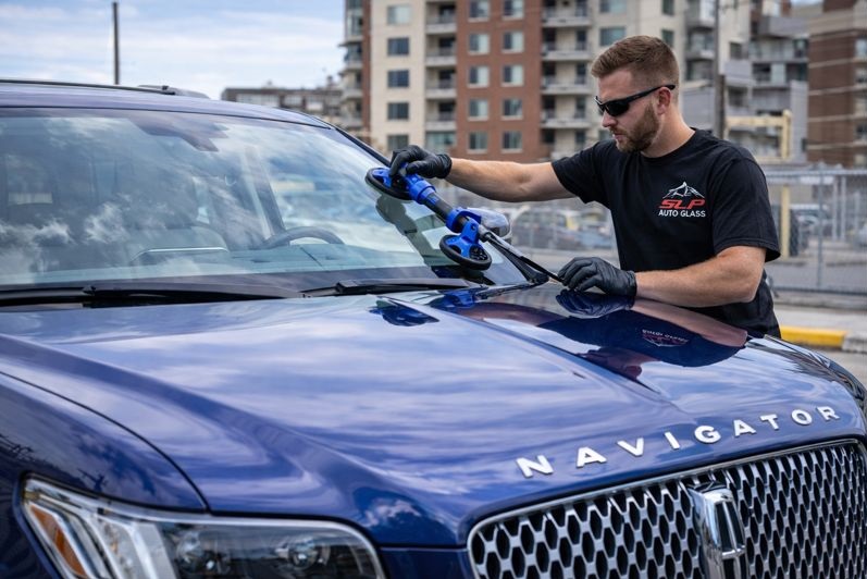 SLP Auto Glass technician replacing the windshield on a blue Lincoln Navigator at an urban service location