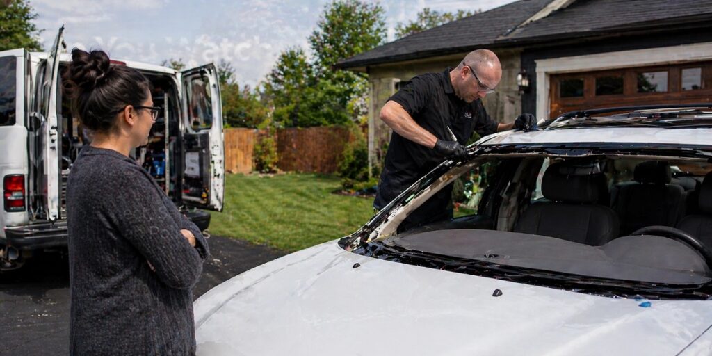 Mobile auto glass technician replacing windshield while customer observes from a safe distance